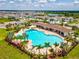 An aerial view of a community pool with lounge chairs, umbrellas, palm trees, and a nearby lake at 33716 Elm Hill Br, Wesley Chapel, FL 33545