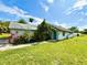 Quaint single-story home featuring a blue door, lush landscaping, and a well-maintained front lawn under a bright, sunny sky at 14318 Guava St, Hudson, FL 34667