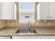 Close-up of the kitchen sink featuring granite countertops, travertine backsplash and white cabinets at 1611 Cresson Ridge Ln, Brandon, FL 33510