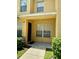 Close-up of the townhouse entrance shows a light-yellow facade, an entry door, and a neatly manicured green bushes at 6333 Maisie Rd, Zephyrhills, FL 33542