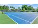 Well-maintained blue and green tennis court with net, surrounded by lush landscaping and tall palm trees at 1806 Powder Ridge Dr, Valrico, FL 33594