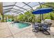 Inviting screened pool area featuring a refreshing pool, relaxing spa, lush greenery, and outdoor dining space at 29118 Picana Ln, Wesley Chapel, FL 33543