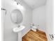 Half bathroom with pedestal sink, round mirror, modern lighting, and wooden floors at 9293 Rally Spring Loop, Wesley Chapel, FL 33545