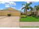 Charming yellow home featuring a two-car garage, well-manicured lawn, and mature palm trees under a clear blue sky at 11559 Captiva Kay Dr, Riverview, FL 33569
