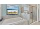 Bright bathroom featuring a soaking tub, glass-enclosed shower, and a window offering serene water views at 11612 Sunburst Marble Rd, Riverview, FL 33579