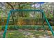 A green metal swing set sits within a lush green lawn, perfect for Gathering fun at 2403 W Sunset Dr, Tampa, FL 33629