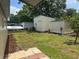 An overgrown backyard featuring multiple storage sheds, patchy grass, and a partial view of a covered vehicle at 116 Cranbrooke Dr, Seffner, FL 33584