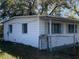 Angled view of the backyard featuring the home's back side, exterior siding, trees, and overgrown vegetation at 1716 Lancelot Loop, Tampa, FL 33619
