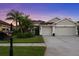Home featuring a 3-car garage and lush landscaping, captured at dusk with purple sky at 10516 Gretna Green Dr, Tampa, FL 33626
