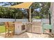 Outdoor kitchen with a stainless steel grill, bar seating, and shade, perfect for entertaining in this backyard space at 1579 Bayshore Blvd, Dunedin, FL 34698