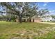 Charming single-story home with arched gate, front yard, and a large mature shade tree in a residential setting at 2410 Covington Ave, Spring Hill, FL 34608