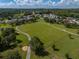 Aerial view of a community featuring a large grassy field, walking path, dog park, and surrounding homes under a partly cloudy sky at 34652 Heavenly Ln, Dade City, FL 33525