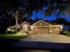 Exterior shot of a three-car garage home showcasing warm exterior lighting and landscaping at twilight at 5704 Eaglemount Cir, Lithia, FL 33547