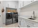 Well-organized laundry room featuring gray washer and dryer, white cabinets, marble counters, and a stainless faucet at 703 Monte Cristo Blvd, Tierra Verde, FL 33715