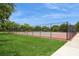 Outdoor tennis court with green and red surfacing, surrounded by a chain-link fence and lush grass at 15801 Cottontail Pl, Tampa, FL 33624