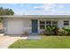 View of home's gray exterior, showing the garage door, blue front door, a landscaped yard, and multi-pane windows at 5961 41St N Ave, St Petersburg, FL 33709