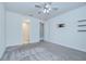 A bright bedroom with gray carpet, ceiling fan, wall mounted shelves and doorways at 6119 Bradford Woods Dr, Zephyrhills, FL 33542