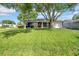 Inviting home featuring lush green lawn, mature trees, and a welcoming red front door at 12401 Yorktown Ln, Bayonet Point, FL 34667
