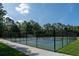 Fenced community tennis court, with lush greenery and trees, under a bright blue sky at 14612 Corkwood Dr, Tampa, FL 33626