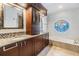 Bathroom featuring dual sinks, granite countertops, wood cabinets, a soaking tub, and a mosaic mirror at 2216 Eagle Bluff Dr, Valrico, FL 33596