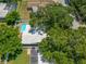 This aerial perspective showcases a sparkling pool beside a quaint single-story home sheltered by mature, leafy trees at 1211 Stony Brook Ln, Dunedin, FL 34698