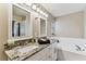 Bright bathroom featuring double sinks, granite countertop, white cabinets, a soaking tub, and contemporary lighting at 8601 Chadwick Dr, Tampa, FL 33635