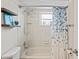 Well-lit bathroom featuring a shower-tub combo with a stylish blue shower curtain and a decorative display shelf at 1038 Shenandoah Ln, Spring Hill, FL 34606
