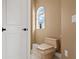 Well-lit, neutral-toned powder room with toilet adjacent to an arched window and closed door at 3236 Gulf Winds Cir, Hernando Beach, FL 34607