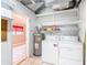 Functional laundry room with washer, dryer, water heater, shelving, and tiled floor, leading to additional space at 4915 Chariton Ave, Tampa, FL 33603