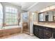 Bright bathroom offers soaking tub under picture window, tiled shower, and dark wood vanity at 16104 Bridgedale Dr, Lithia, FL 33547