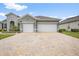A home showcasing a spacious two-car garage and brick driveway, enhanced by landscaping and neutral color palette at 19819 Tattnall Way, Brooksville, FL 34601