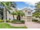 Two-story tan house featuring an attached two car garage and lush landscaping with palm trees at 2354 Messenger Cir, Safety Harbor, FL 34695