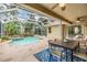 A covered patio features an inviting dining area with views of the screened pool, spa, waterfall, and lush landscaping at 2354 Messenger Cir, Safety Harbor, FL 34695