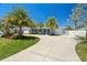 Inviting single-story home with manicured lawn, mature palm trees, and a lengthy drive leading to a single car garage at 9485 Treasure Ne Ln, St Petersburg, FL 33702