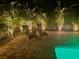 Outdoor pool area with two lounge chairs, palm trees, and paver deck illuminated with warm lighting at 9591 Commodore Dr, Seminole, FL 33776