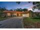 Charming single-story home featuring a stone facade, lush landscaping, and a long driveway leading to an attached garage at dusk at 3041 Oak View Dr, Palm Harbor, FL 34684