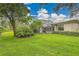 Backyard featuring a screened lanai, green grass, mature trees, and landscaping at 3207 Hilltop Ln, Largo, FL 33770