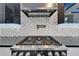 Close up of modern gas cooktop with stainless hood vent and unique backsplash at 6520 Simone Shores Cir, Apollo Beach, FL 33572