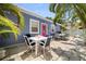 Blue cottage with pink door boasts a stone patio with outdoor dining, palm trees, and a glimpse of the pool at 722 Gulf Blvd, Indian Rocks Beach, FL 33785