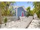 Charming blue cottage exterior features a pink door, white picket fence, tropical landscaping, and a patio seating area at 722 Gulf Blvd, Indian Rocks Beach, FL 33785