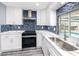 Close-up of modern kitchen features white cabinets, stainless steel appliances, quartz countertops, and blue tiled backsplash at 9909 San Mateo Way, Port Richey, FL 34668