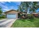 Single-story home featuring a large palm tree, landscaped front yard and a two-car garage at 1281 Amberlea E Dr, Dunedin, FL 34698