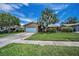 Single-story home featuring lush landscaping, a large palm tree, and a two-car garage at 1281 Amberlea E Dr, Dunedin, FL 34698