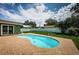 Backyard showcases a kidney-shaped pool with surrounding brick, a green lawn, and a white fence at 12873 Cumberland Dr, Largo, FL 33773