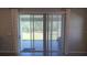 An outdoor patio is shown through sliding glass doors with custom curtains and vertical blinds, offering a seamless indoor-outdoor transition at 13111 Pepper Stem St, Spring Hill, FL 34609