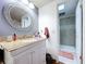 Bathroom featuring modern vanity, granite countertop, and decorative round mirror with a step-in shower in the background at 1902 Rebecca Rd, Lutz, FL 33548