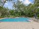 Large community pool surrounded by trees, lounge chairs, and dining tables under umbrellas at 3062 Eastland Blvd # 405, Clearwater, FL 33761