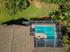 Aerial view of a screened in pool and patio with brown shingles and lush green trees at 4133 Auston Way, Palm Harbor, FL 34685