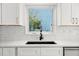 Modern kitchen featuring white cabinets, marble backsplash, and a stainless steel sink with a view of the outdoors at 600 115Th Ave, Treasure Island, FL 33706