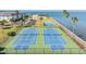 Aerial view of multiple blue tennis courts, fenced in, and palm trees nearby a building and the water at 7 Elgin Pl # 202, Dunedin, FL 34698